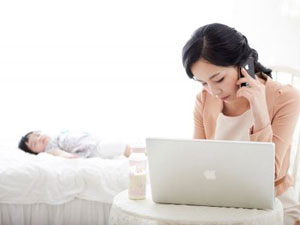 침대 위에 잠들어 있는 아기와 전화 통화중인 엄마